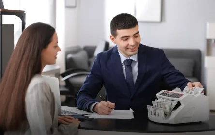 The-Importance-of-Automated-Cash-Reconciliation-Tools.webp A man and woman discussing cash reconciliation while using a counting machine, emphasizing the benefits of automated cash handling.